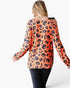 A woman shown from the back wearing a long-sleeve cold-shoulder top with an orange base and a black pumpkin print, paired with dark jeans against a plain white background.