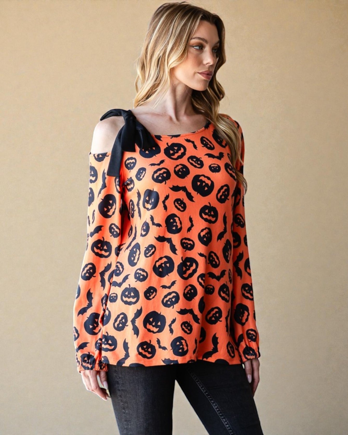Woman wearing an orange long-sleeve top with black Halloween-themed pattern against a beige background