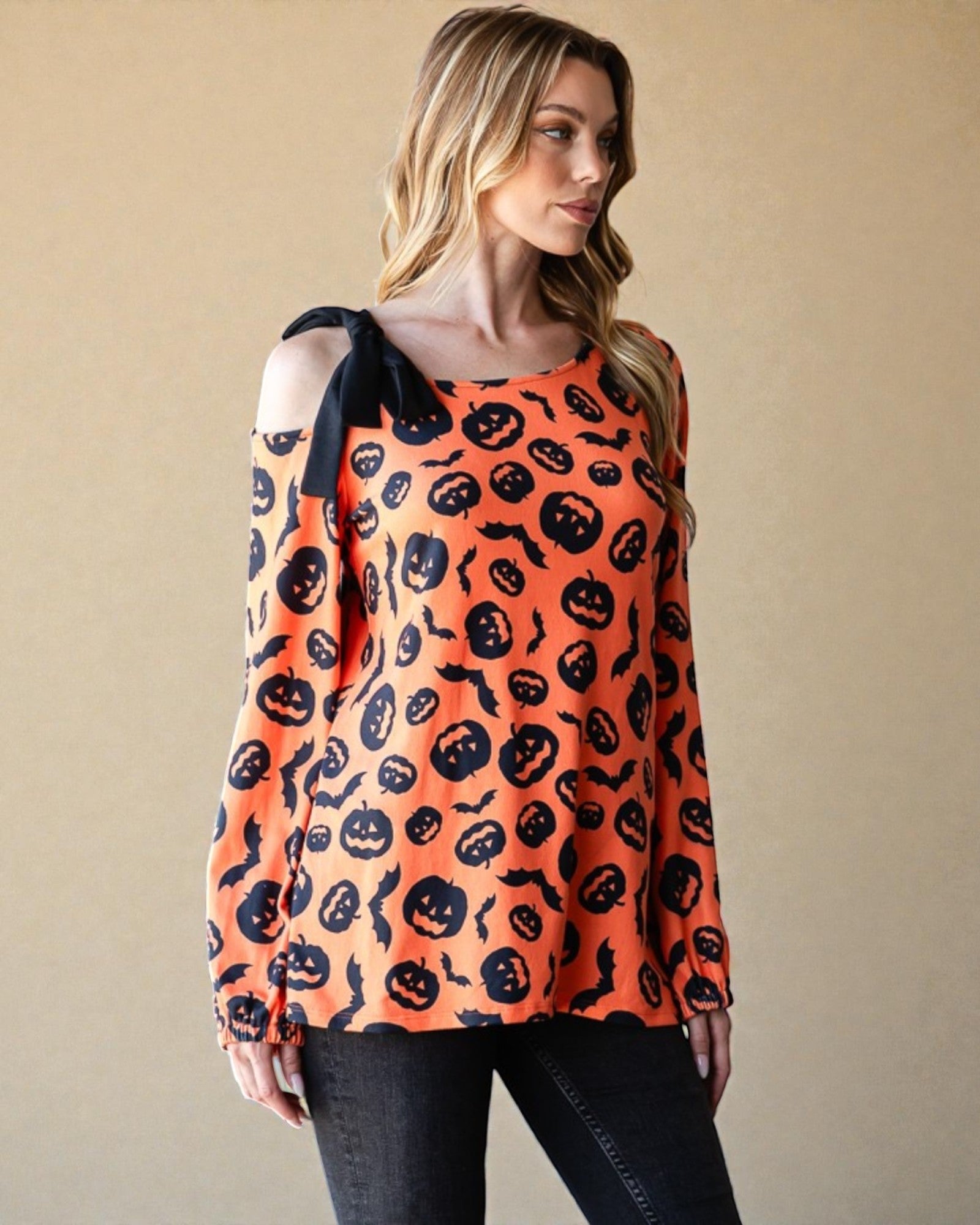 Woman wearing an orange long-sleeve top with black Halloween-themed pattern against a beige background