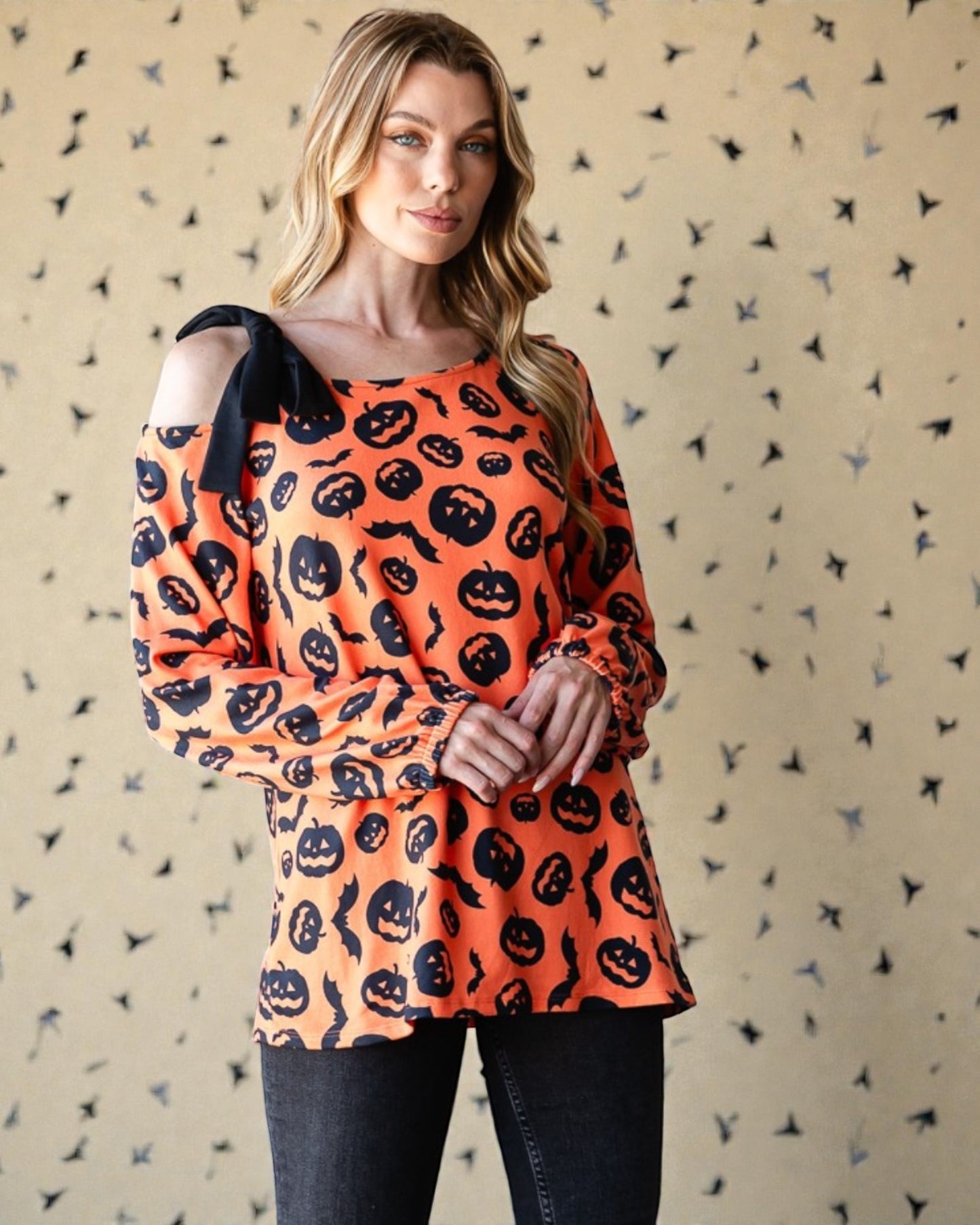 Woman wearing an orange Halloween-themed top with black patterns against a patterned background