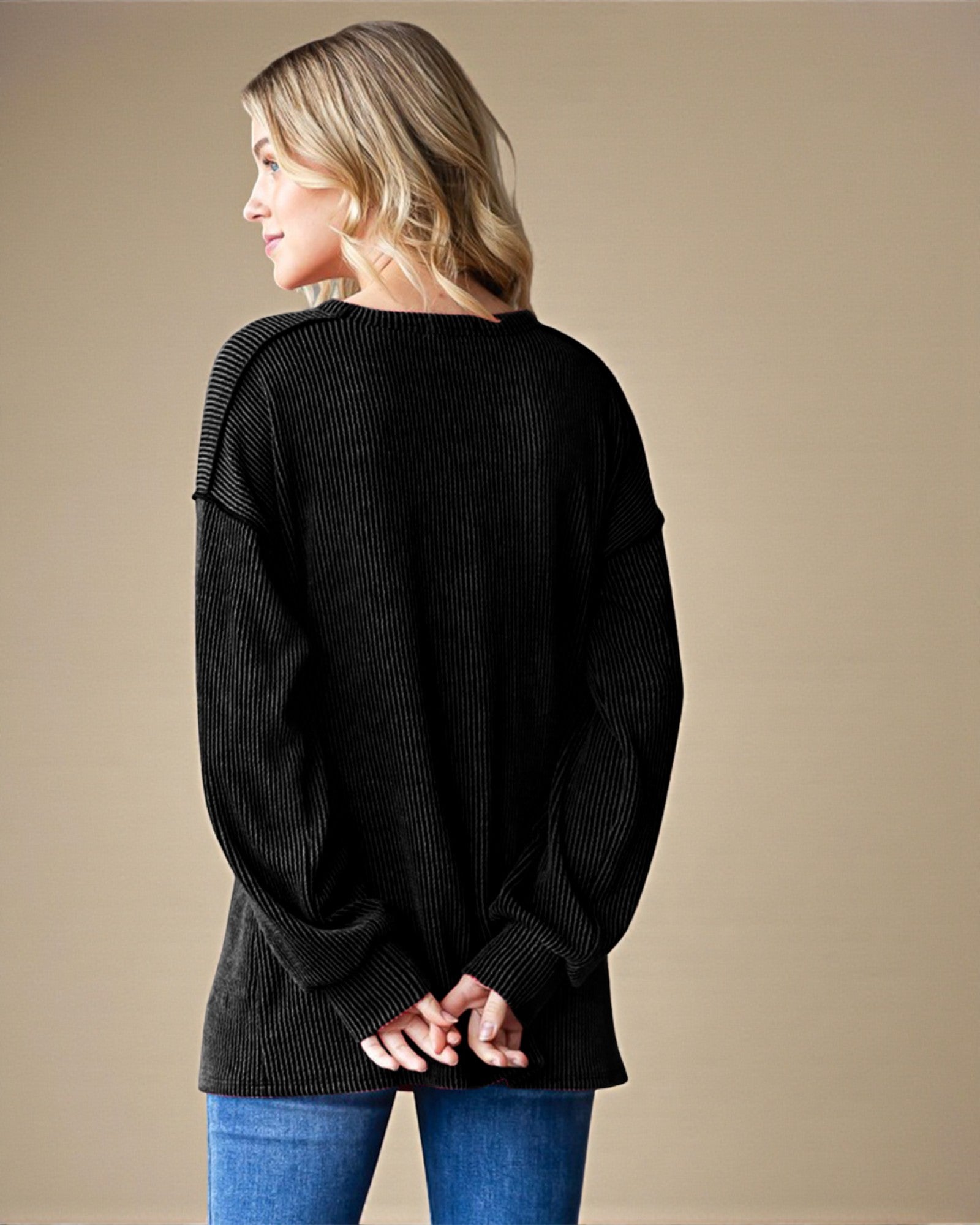 Woman wearing a black sweater and blue jeans against a beige background