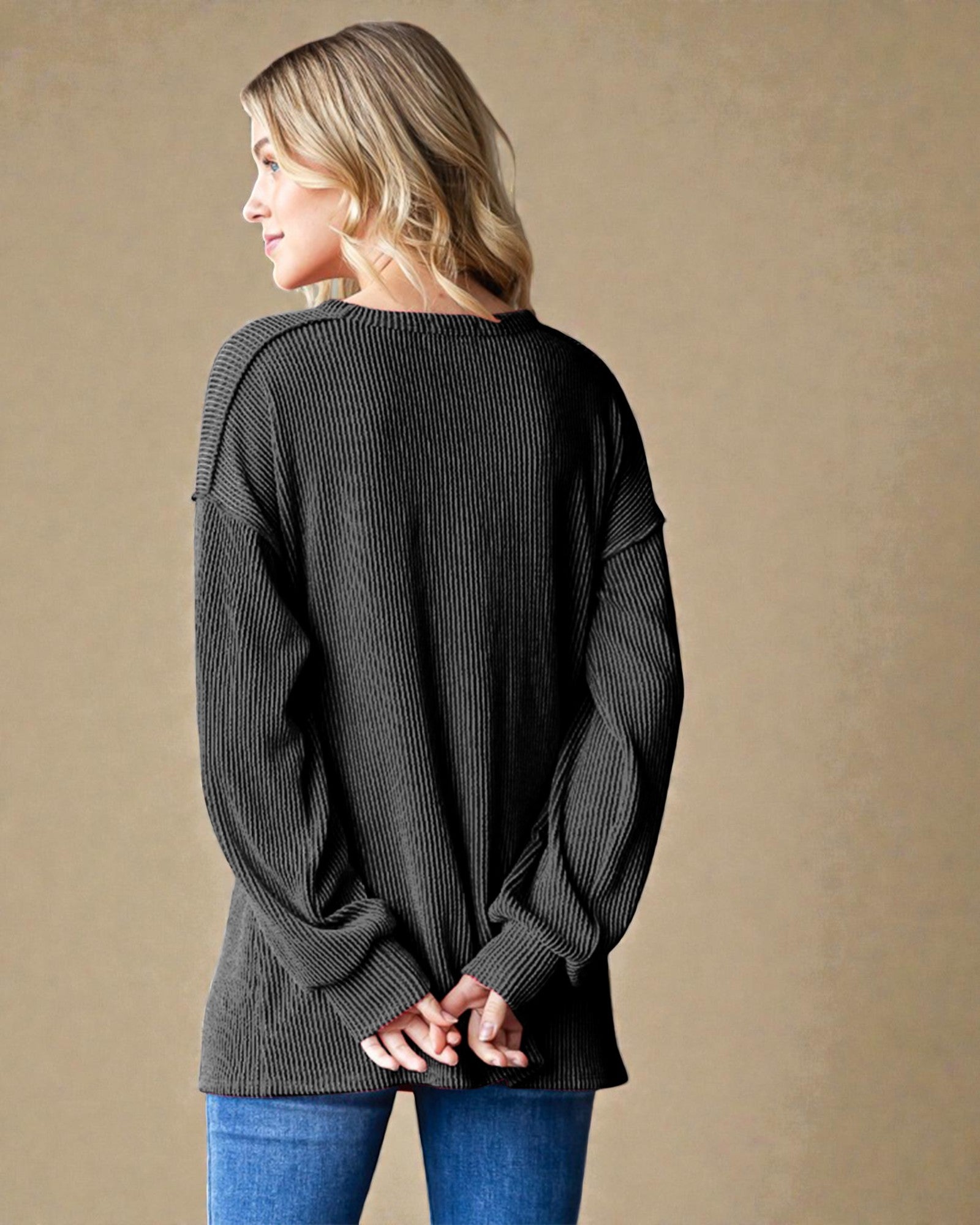 Woman wearing a dark gray ribbed sweater against a beige background
