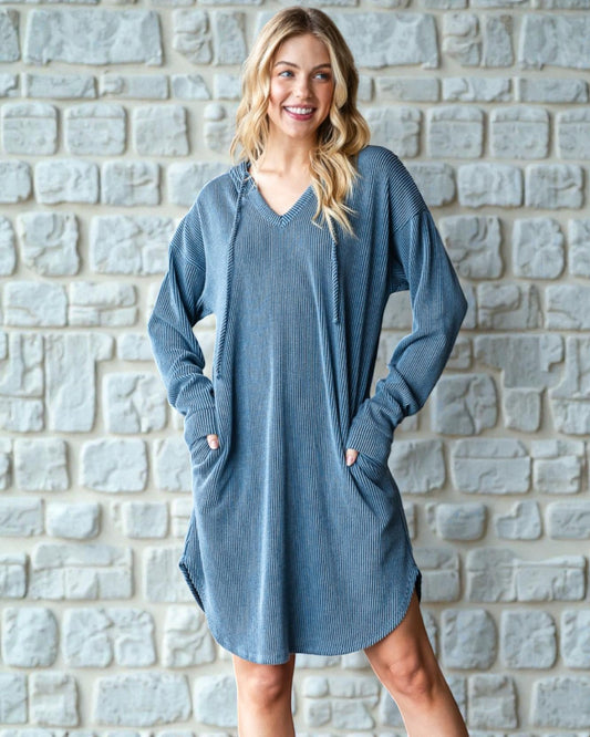 Woman wearing a blue sweater dress standing against a stone wall.