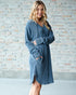 Woman wearing a blue sweater dress against a brick wall.