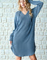Woman wearing a blue ribbed dress against a textured white wall