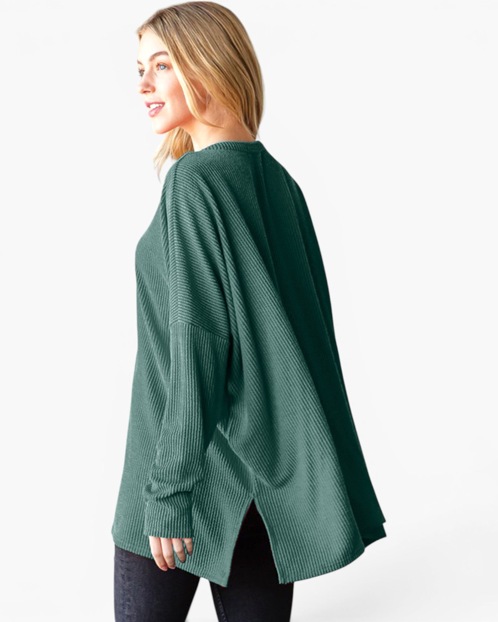 A woman wearing an oversized, long-sleeve ribbed knit sweater in forest green, shown from a side-back angle against a plain white studio background.