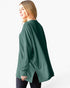 A woman wearing an oversized, long-sleeve ribbed knit sweater in forest green, shown from a side-back angle against a plain white studio background.