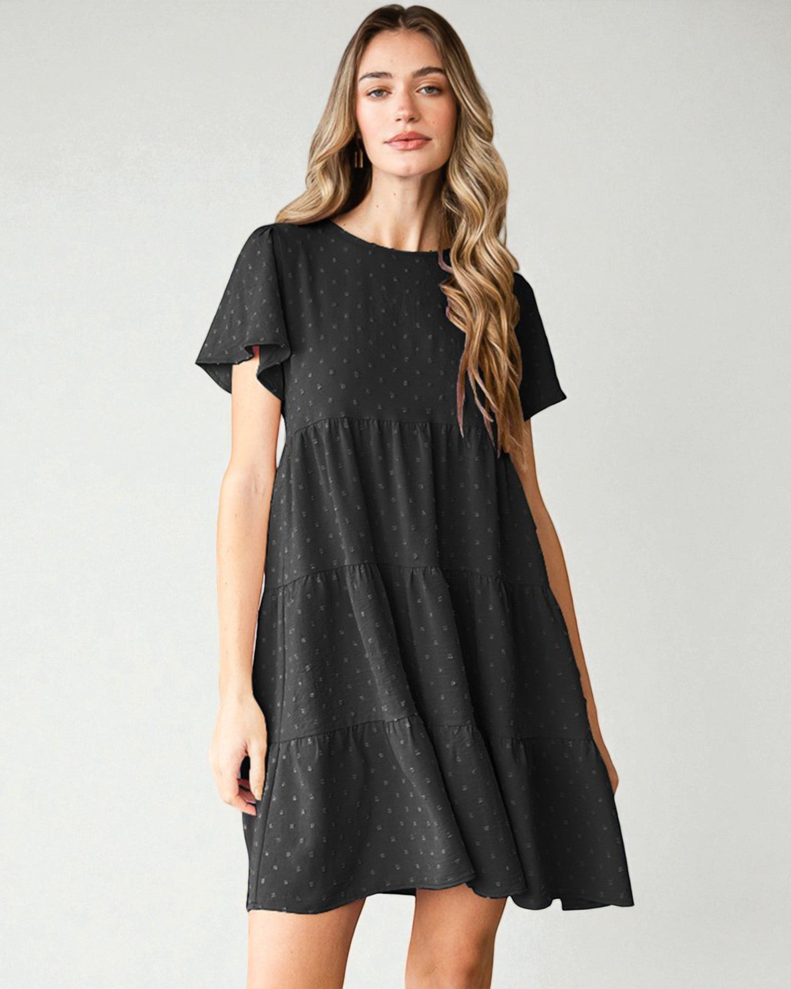 Woman wearing a black tiered dress against a plain background