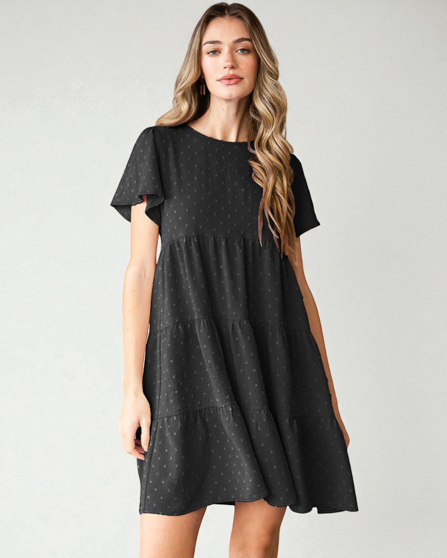 Woman wearing a black tiered dress against a plain background