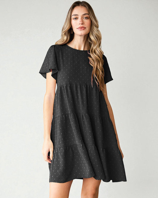 Woman wearing a black tiered dress against a plain background