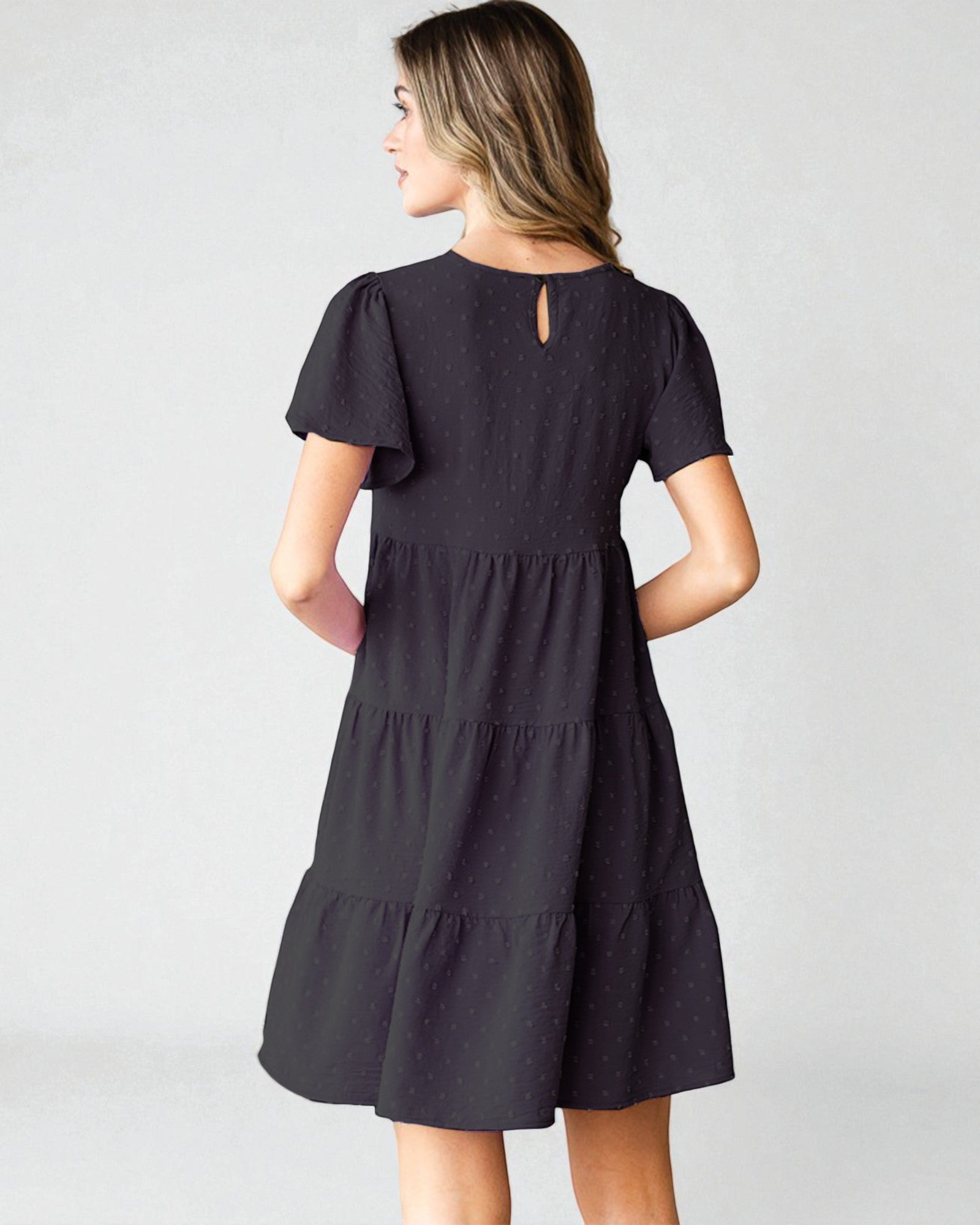 Woman wearing a black dress with ruffled sleeves and tiered skirt on a white background