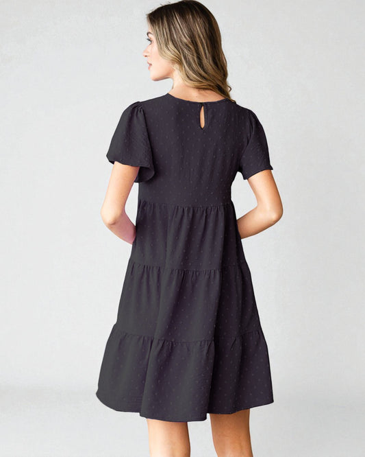 Woman wearing a black dress with ruffled sleeves and tiered skirt on a white background