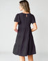 Woman wearing a black dress with ruffled sleeves and tiered skirt on a white background