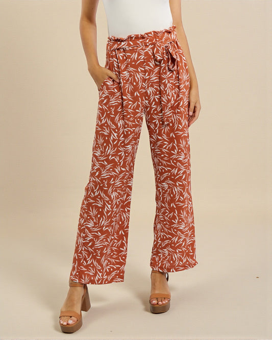 Person wearing rust-colored leaf-patterned pants on a beige background