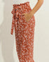 Brown pants with white leaf pattern worn by a person on a plain background