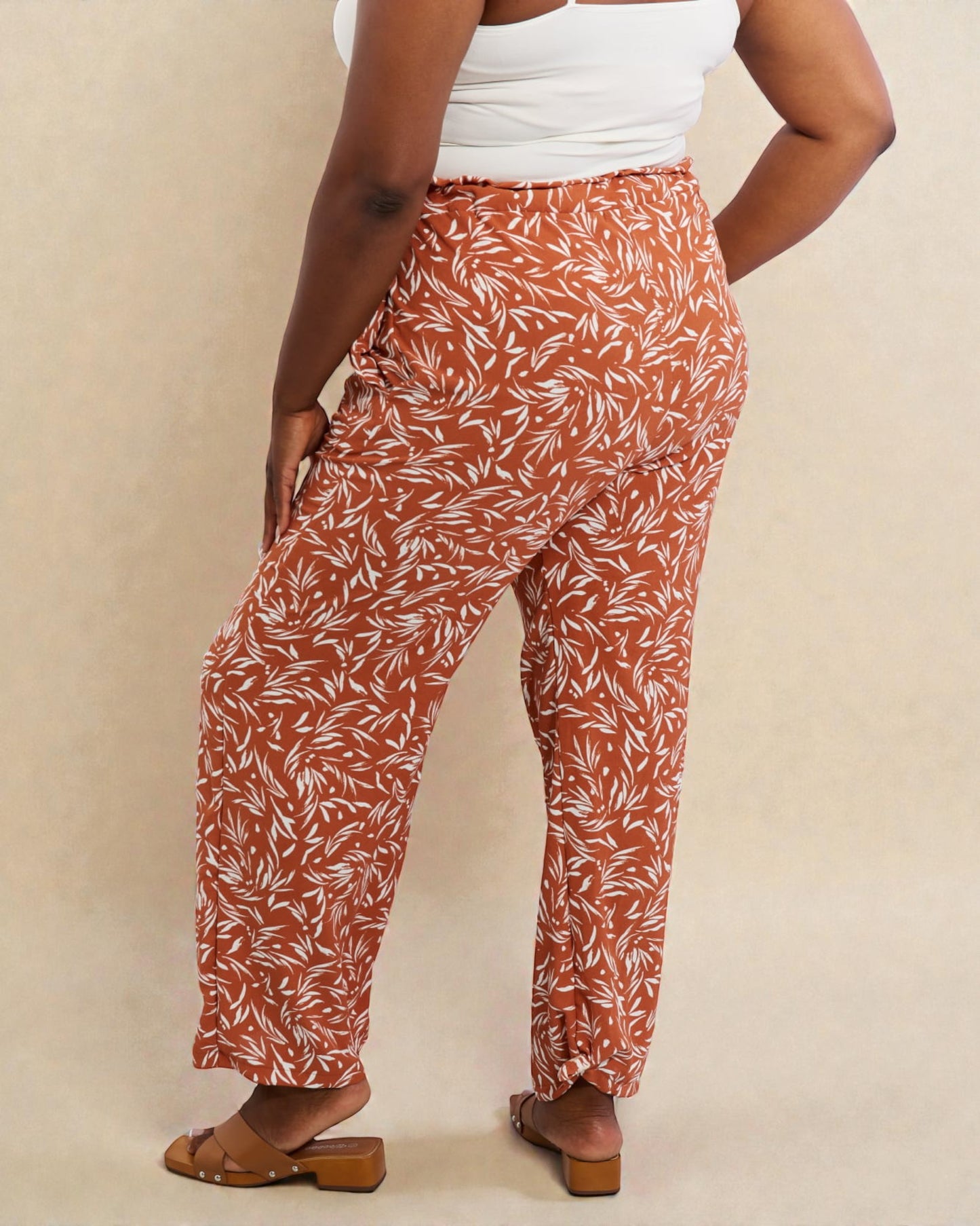 Person wearing rust-colored pants with a white leaf pattern on a beige background