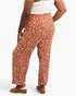 A person shown from the back wearing wide-leg rust-orange pants with a white leaf print, paired with a white top and brown sandals, against a light gray studio background.