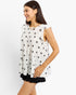 A woman wearing a sleeveless white pleated top with a black star pattern and a black ruffled hem, photographed against a light gray studio background.