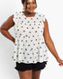 A woman wearing a white sleeveless ruffle-sleeve top with an all-over black star pattern and black ruffled shorts, photographed against a light gray studio background.