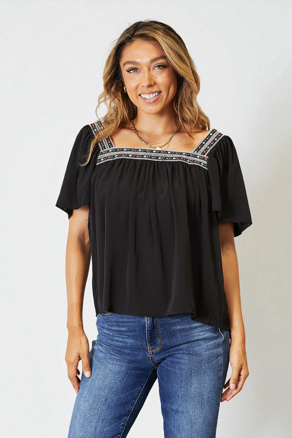 Woman wearing a black top with ruffled sleeves and blue jeans on a white background