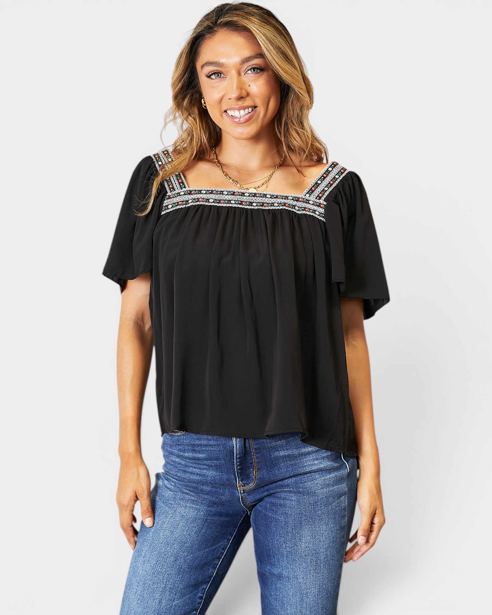 Woman wearing a black top with decorative trim and blue jeans on a white background