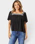 Woman wearing a black top with decorative trim and blue jeans on a white background