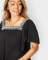 Woman wearing a black top with decorative neckline on a white background