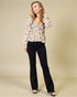 Woman wearing a floral blouse and black pants on a beige background