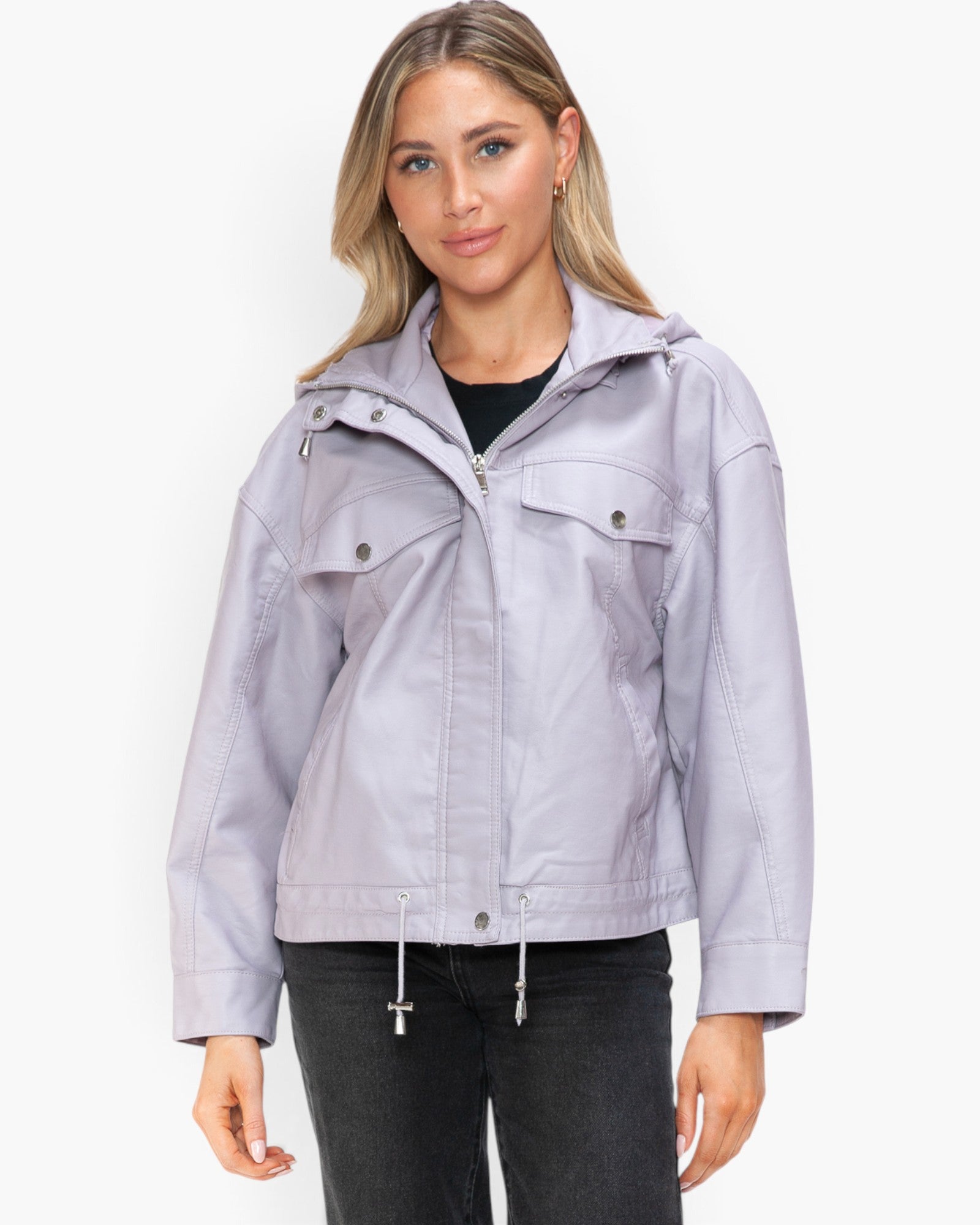 A woman modeling a light lavender hooded jacket with a front zipper, snap-button chest flap pockets, and drawstring hem, paired with a black top and dark jeans against a plain white studio background.
