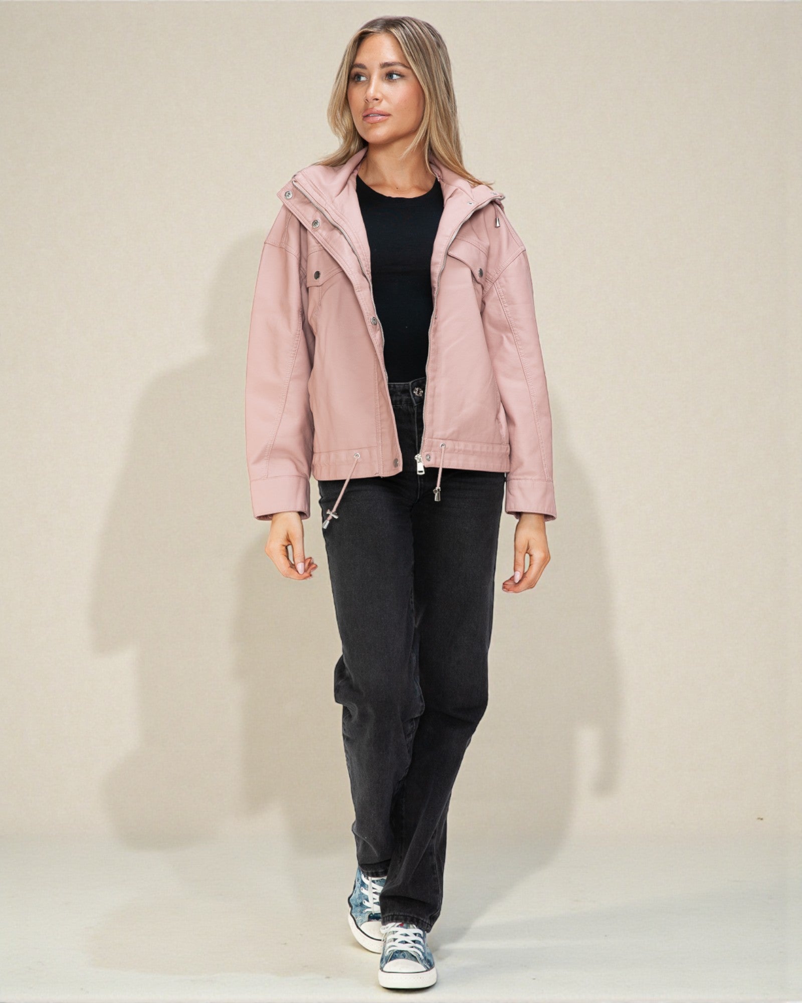 Woman wearing a pink jacket and black pants on a plain background