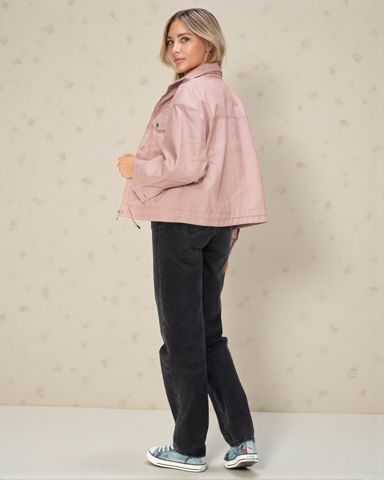 Woman wearing a pink jacket and black pants against a beige background