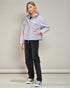 Woman wearing a light gray jacket and black pants against a plain background