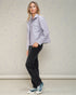 Woman wearing a light gray jacket, black jeans, and blue sneakers against a plain background