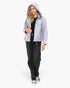 A woman modeling a light lavender hooded jacket over a black top and black jeans, standing against a plain white studio background.