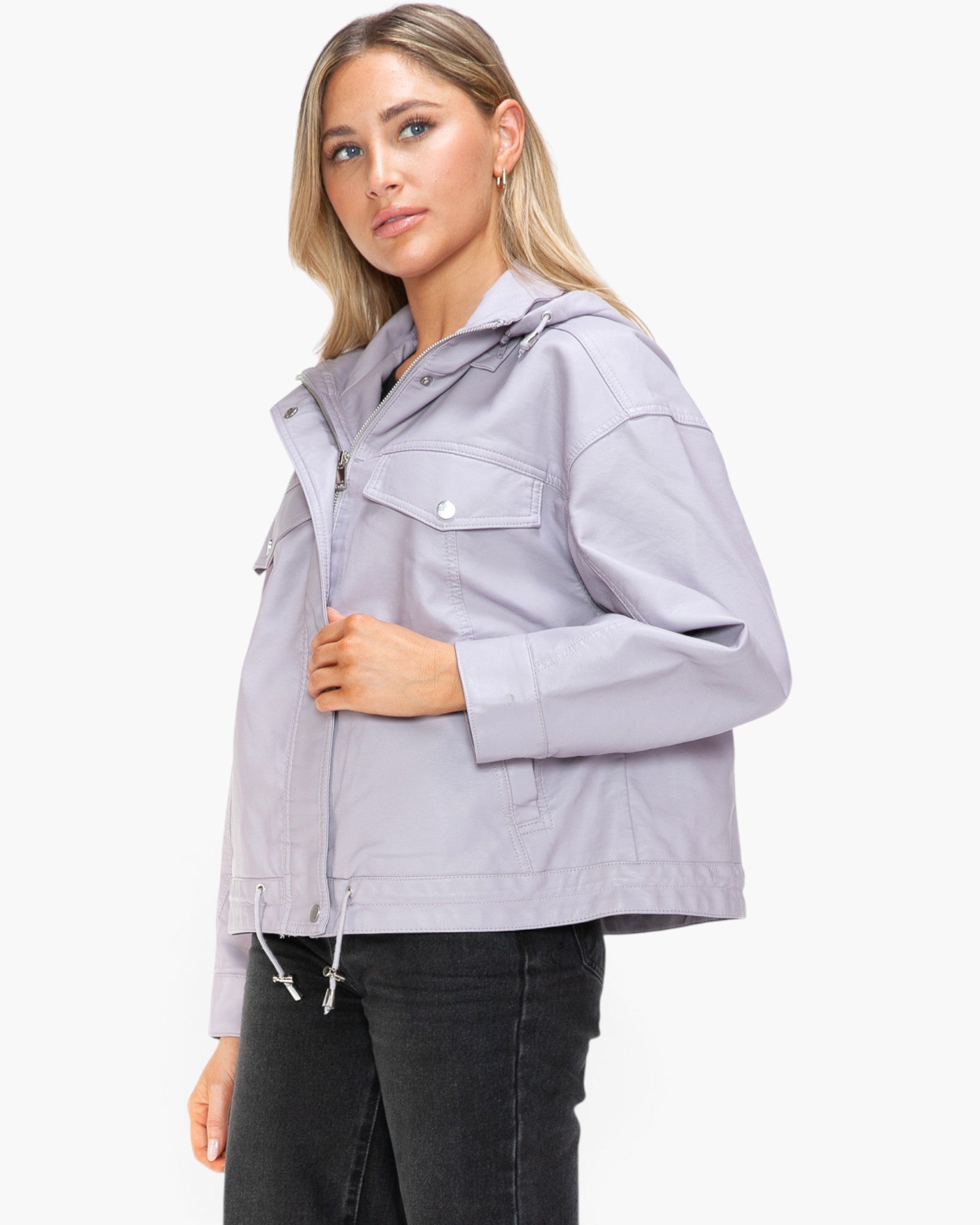 A woman modeling a light lavender utility jacket with a high collar, front zipper, and chest flap pocket, paired with black jeans against a plain white background.