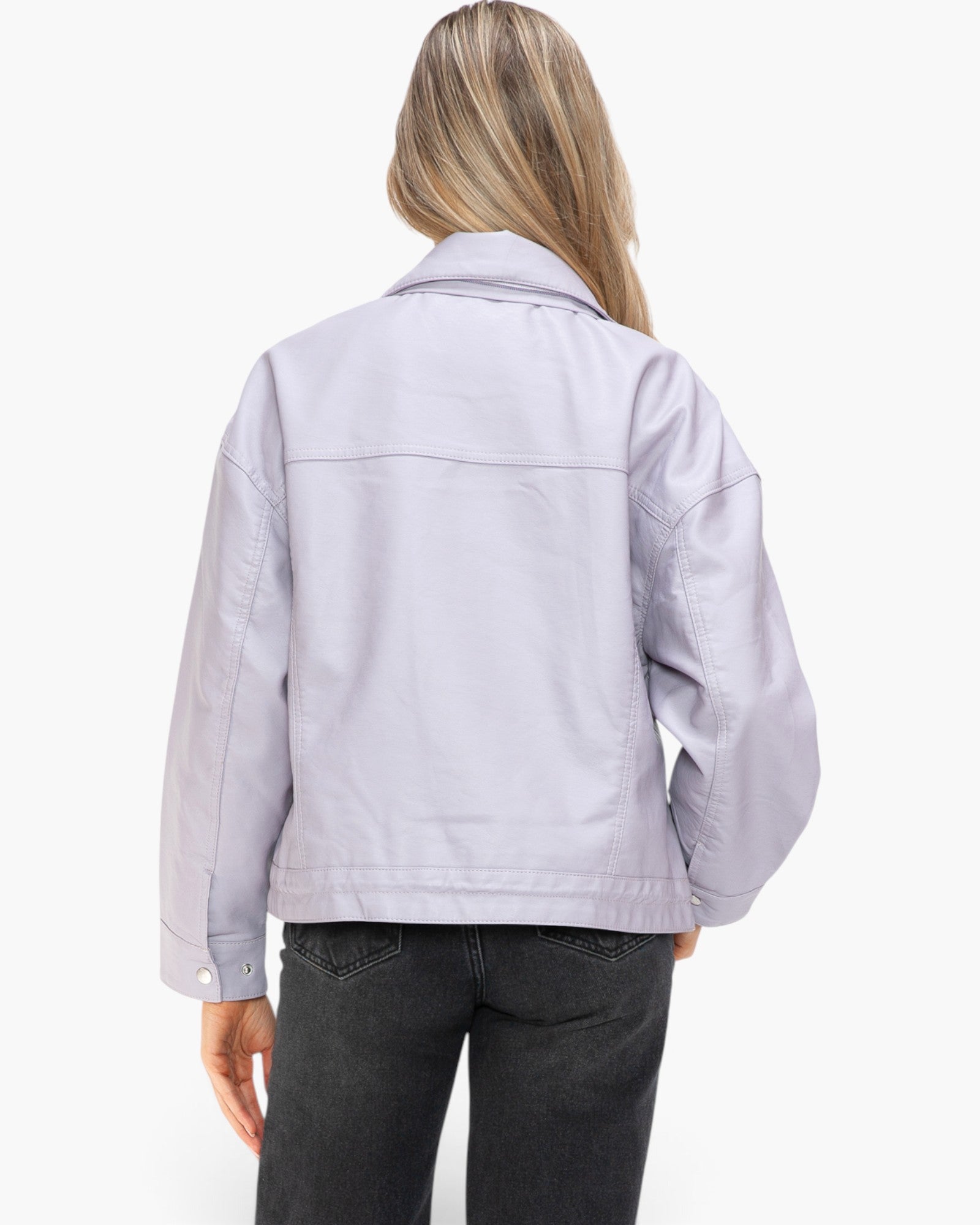 A woman viewed from the back wearing a light lavender-gray utility jacket and dark gray jeans against a plain white studio background.