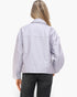 A woman viewed from the back wearing a light lavender-gray utility jacket and dark gray jeans against a plain white studio background.