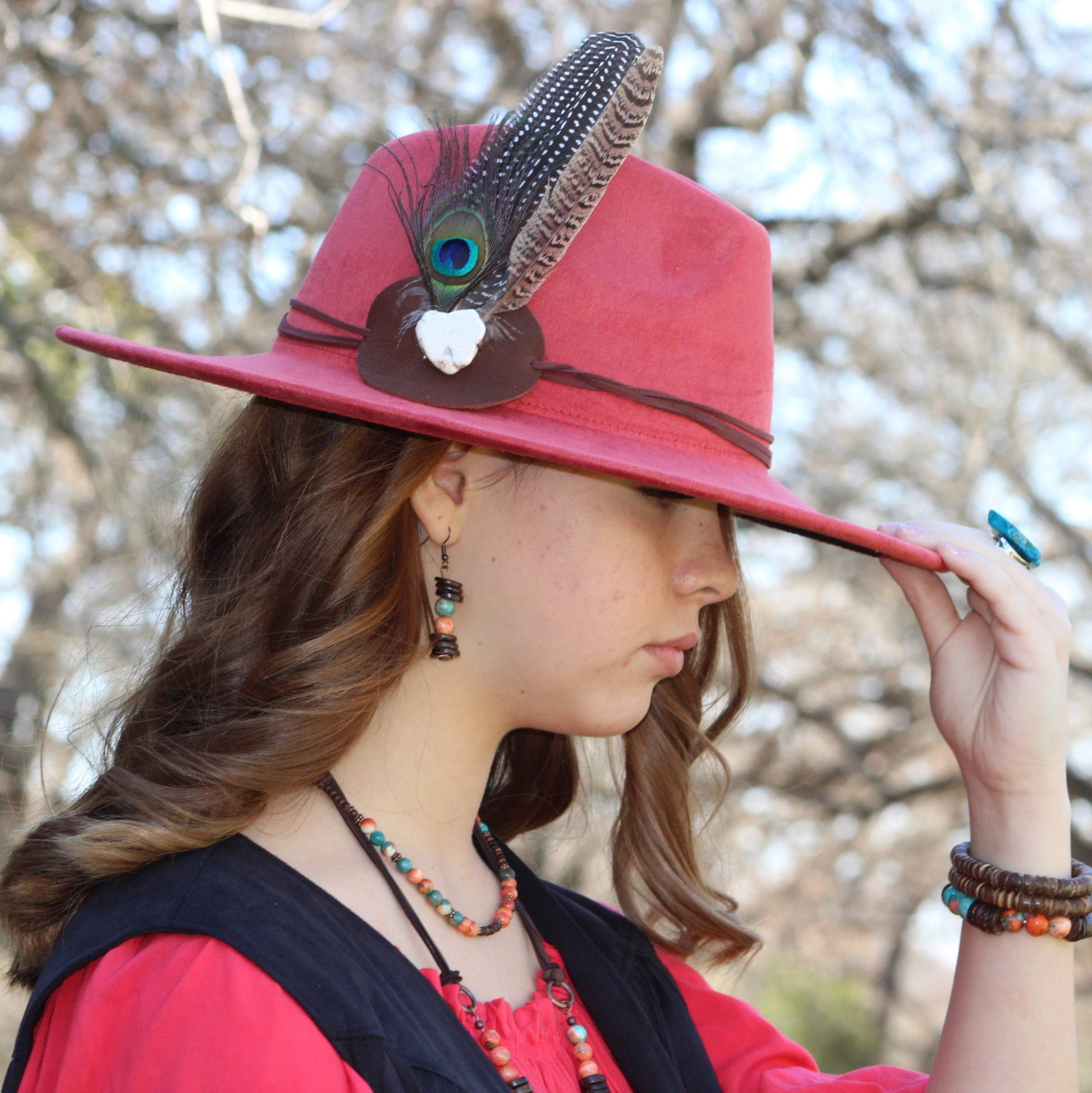 Woman wearing a pink hat with decorative elements, standing outdoors with blurred trees in the background.
