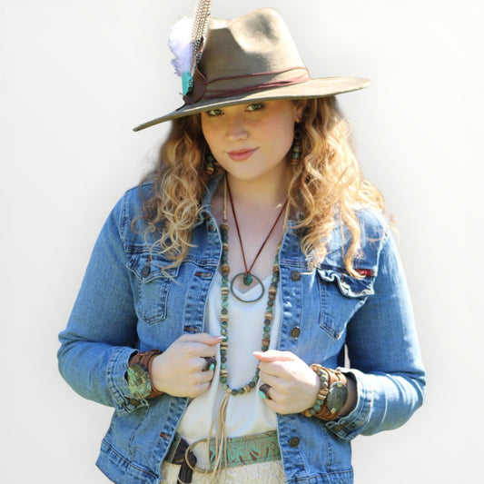 Woman wearing a denim jacket, hat, and multiple necklaces against a white background