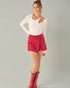 Woman wearing a white long-sleeve top and red skirt with matching boots on a gray background