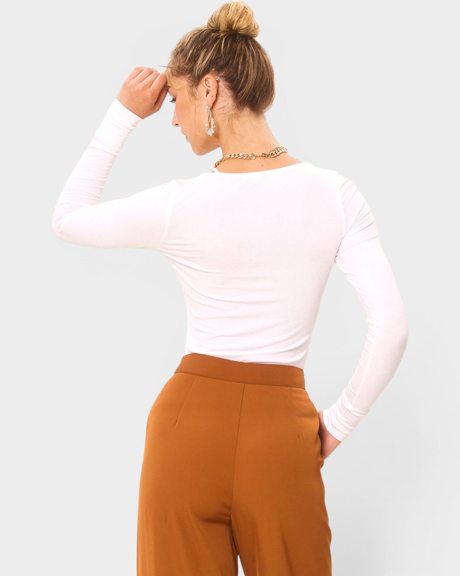 Person wearing a white long-sleeve top and brown pants on a light gray background