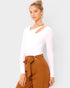 Woman wearing a white long-sleeve top and brown pants with a belt against a plain background