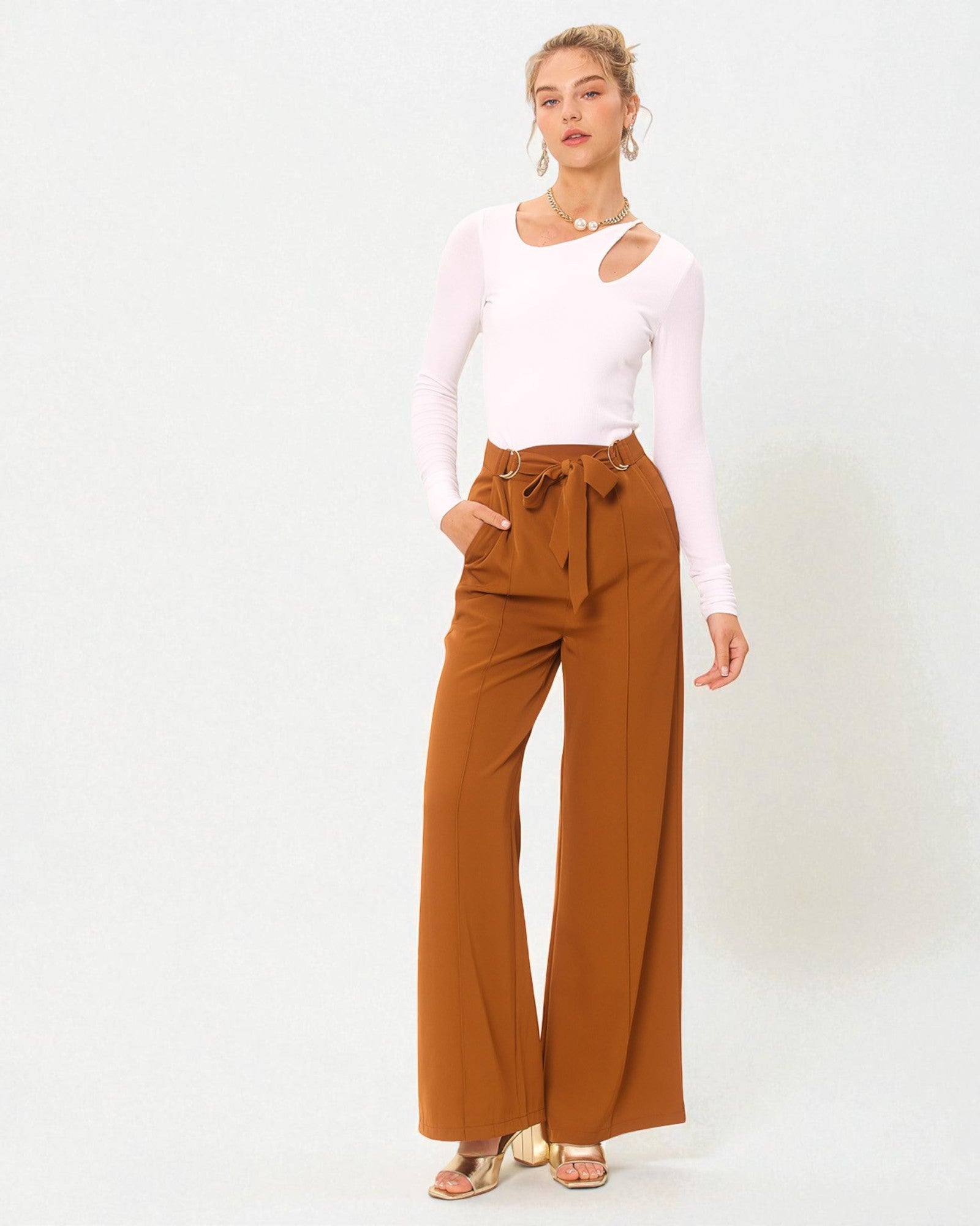 Woman wearing a white long-sleeve top and brown wide-leg pants on a white background