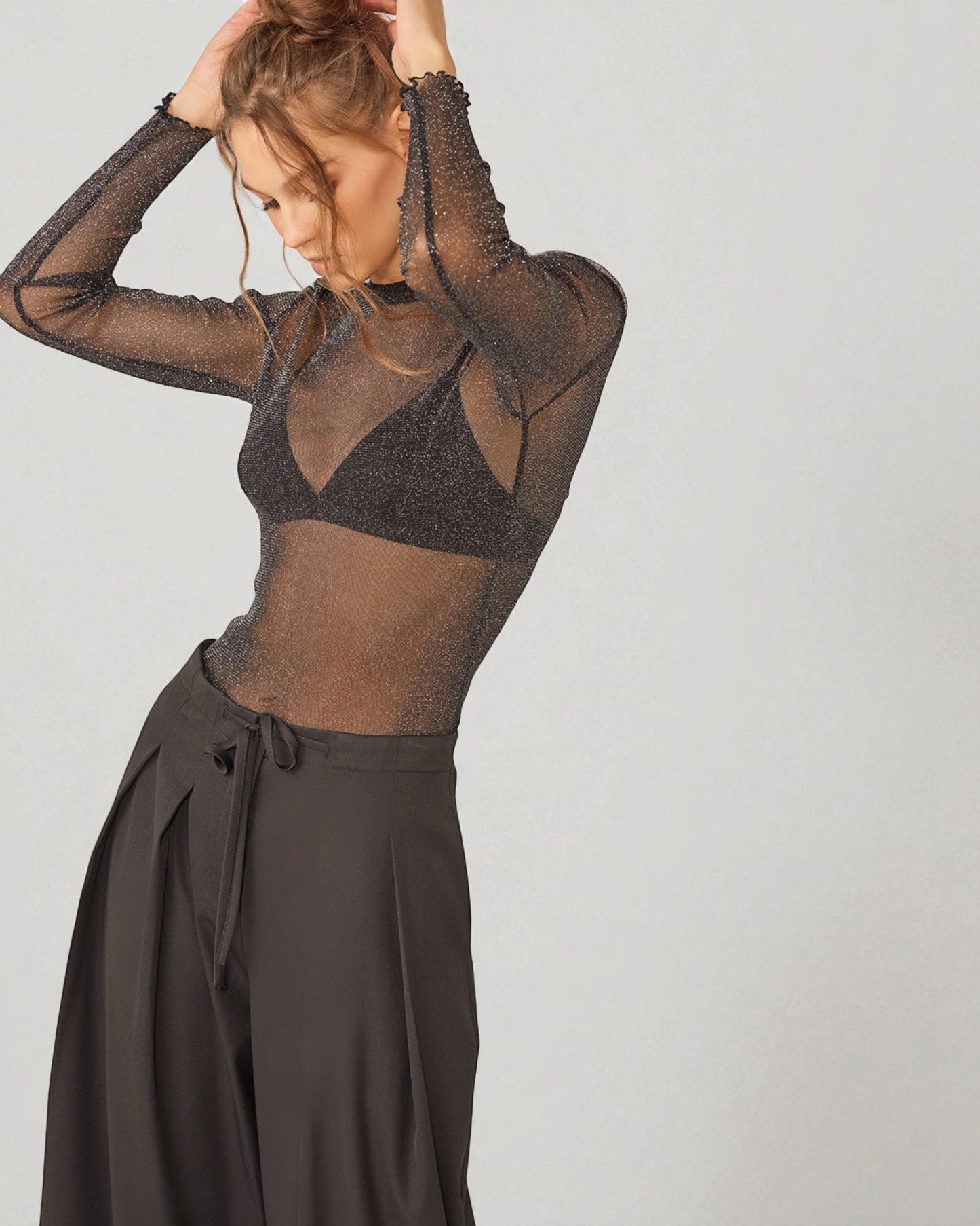 Person wearing a sheer black top and dark pants on a plain background