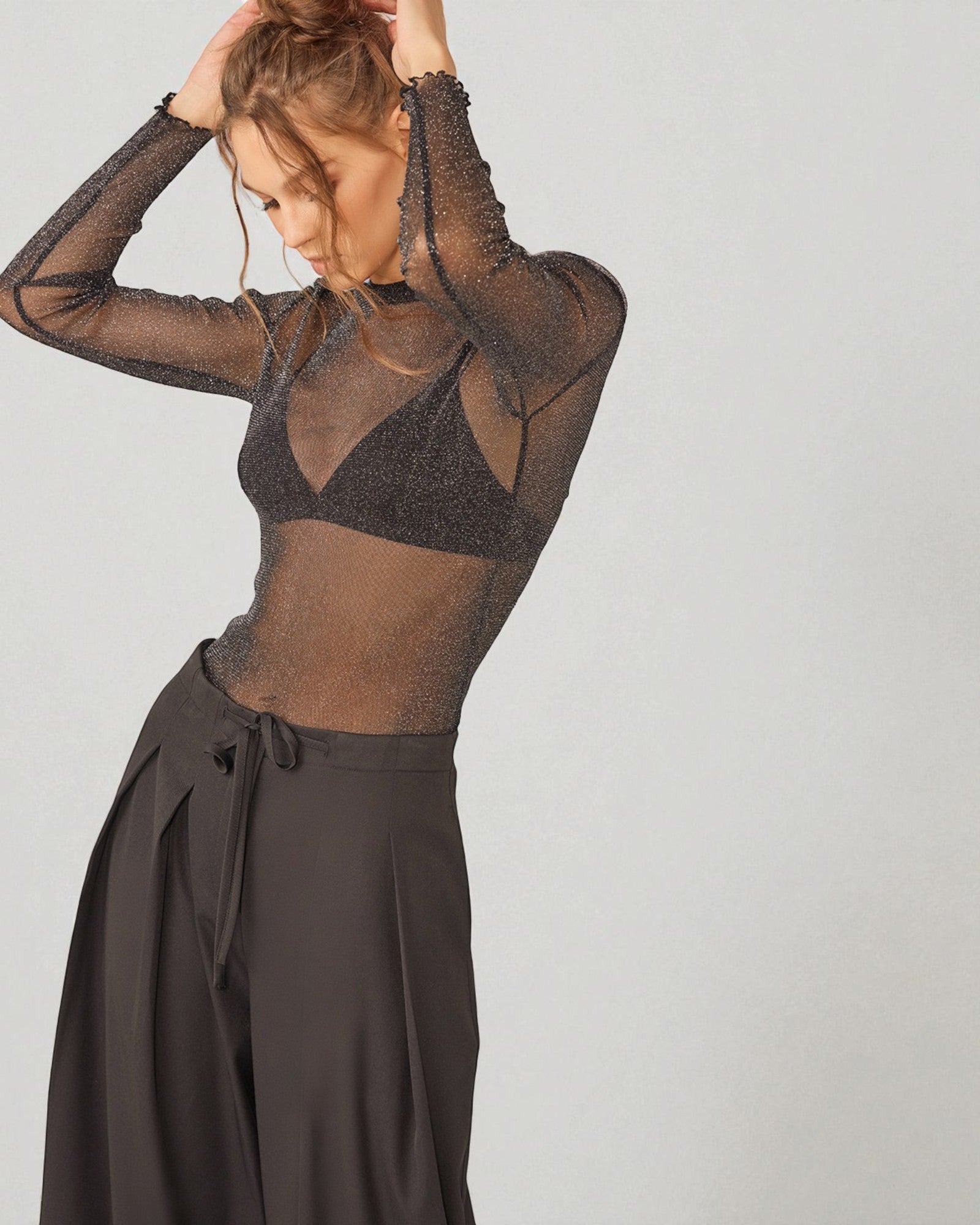 Person wearing a sheer black top and dark pants on a plain background