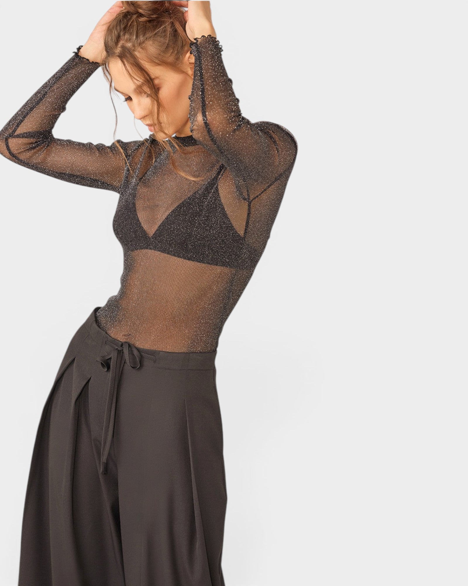 Woman wearing a sheer black long-sleeve top and black skirt on a white background