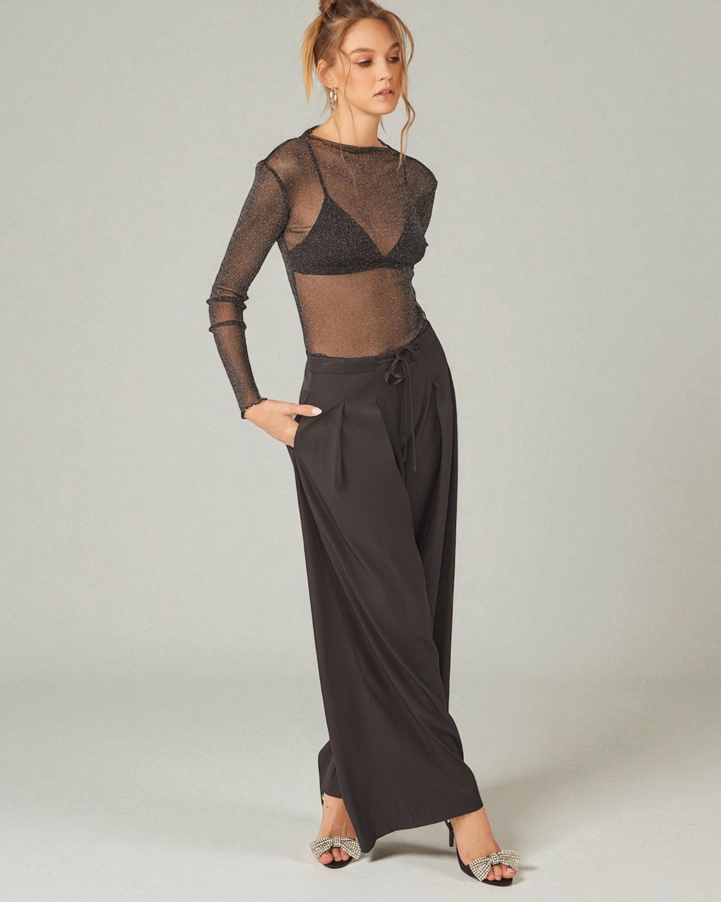 Woman wearing a sheer black top and wide-leg pants on a plain background
