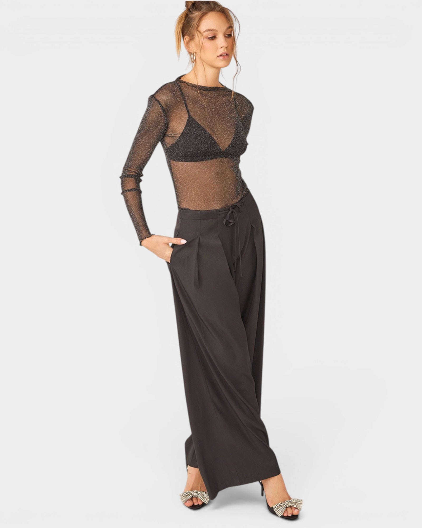 Woman wearing a sheer black top and wide-leg pants on a white background
