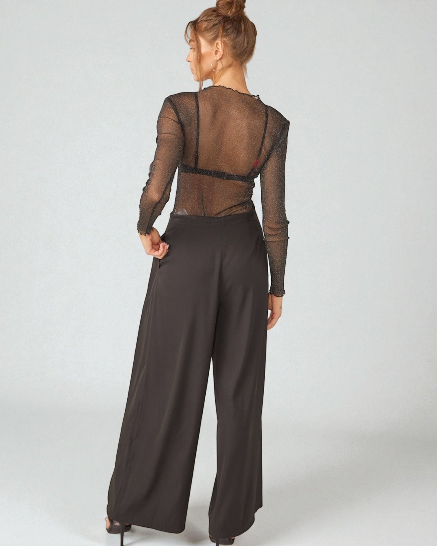 Woman wearing a brown sheer top and wide-leg pants on a white background