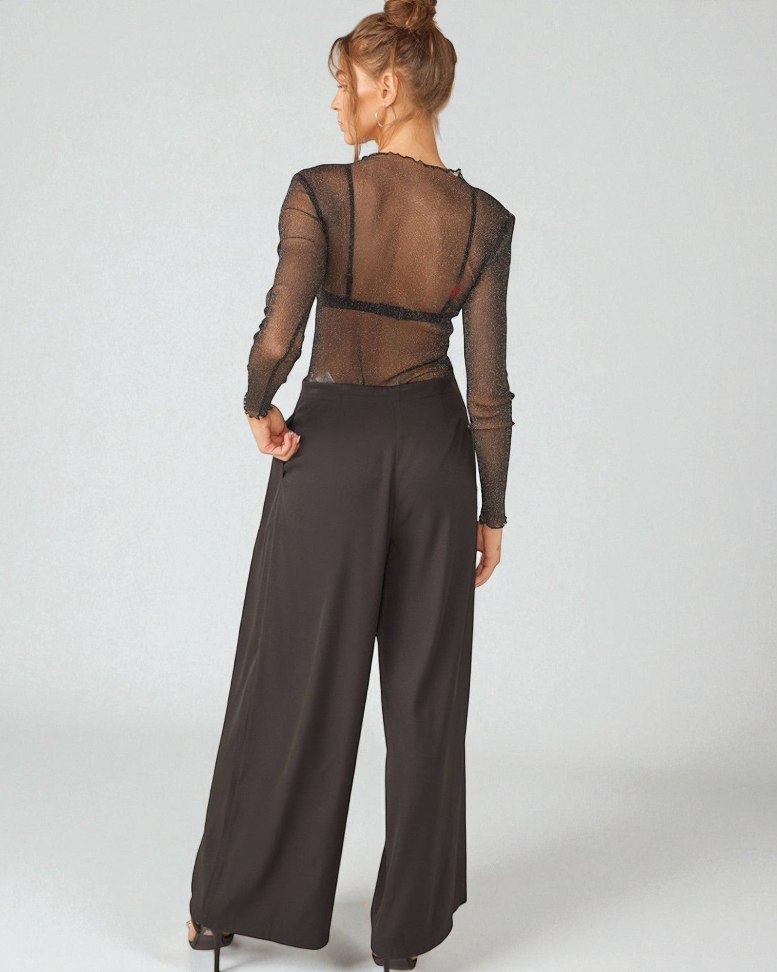 Woman wearing a brown sheer top and wide-leg pants on a white background